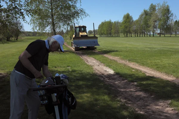 A golf course worker does his job despite a man playing golf ...