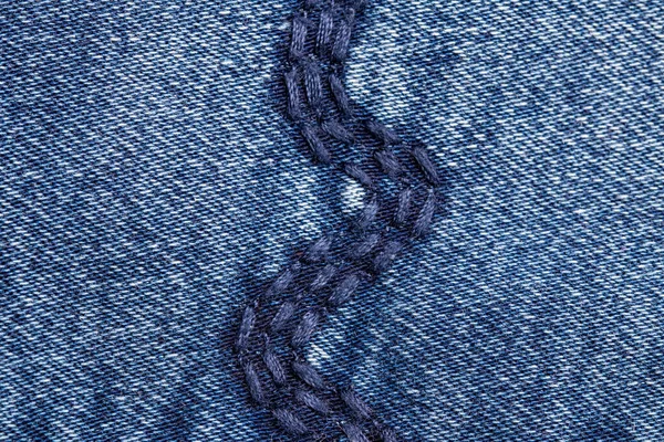 Denim background texture. Close-up of details of a light blue jeans fabric jean surface with fashion embroidery in blue colours. Macro. Top view. Beautiful backdrop with space.