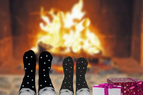 A couple with Christmas wool socks and gift boxes sitting relaxed and comfortable inside near fireplace on a winter night. Winter and xmas holidays and New year concept.