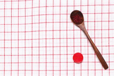 Safran geçmişi. Kırmızı safran baharat iplikleri ya da rustik ahşap kaşıkta iplikler ve kırmızı kareli peçetede safran depolamak için plastik bir kavanoz. Boşluk.