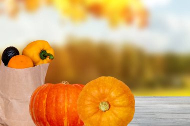 Masanın üzerinde taze sebzeler ve iki balkabağı bulunan kahverengi bir alışveriş çantasının soyut bulanık sonbahar arkaplanı. Yemek ve ürün montajı için yer var. Bağışıklık sisteminin güçlendirilmesi kavramı.