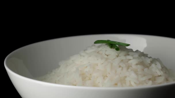 Vařená rýže v bílém talíři se zelenou cibulí na černém pozadí. — Stock video