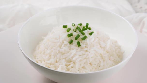 Cooked rice in white plate with green onions on white background. — Stock Video