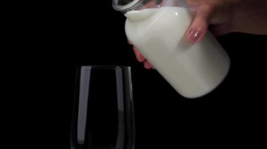 Siyah arka plandaki bir şişeden bardağa süt dökmek. Boşluğu kopyala.