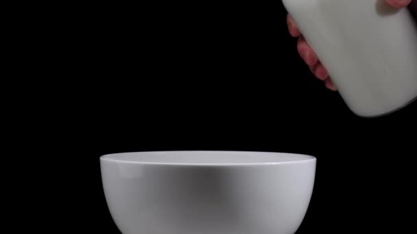 Pouring milk into a bowl on black background. Copy space. Slow motion. — Stock Video