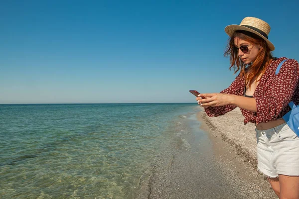 Młoda Kobieta Kapeluszu Okularach Słonecznych Fotografuje Morze Latem Brzegu — Zdjęcie stockowe