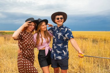 Bir grup kadın ve erkek, yazın mavi gökyüzü ve sarı bir tarlanın arka planında fotoğraflanır.