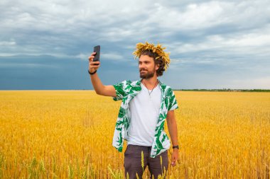 Kafasında tümsek çelengi olan bir adam sarı bir tarlanın arka planında ve yedi yaz gökyüzünde