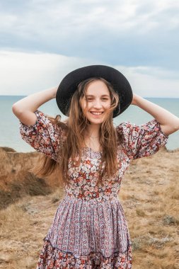 Yazın denize bakan, kanyonun kenarında siyah şapkalı kadın.