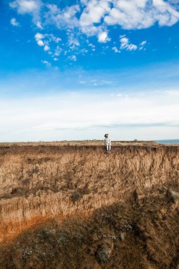 Sakallı bir adam yazın bacakları sarkık bir uçurumun kenarında oturur.