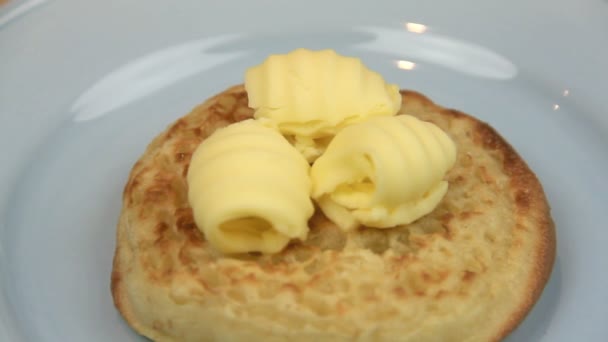 Curls of butter being being spread on a hot English crumpet with a knife. — Stockvideo