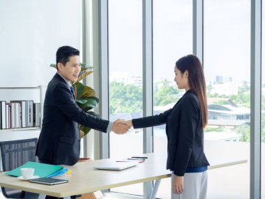 Takım elbiseli Asyalı işadamı ve ofiste tokalaşan iş kadını. Ofisinde masasında duran gülümseyen müdür genç bir bayanla tokalaşıyor, iş görüşmesinden sonra iş başvurusu yapıyor..