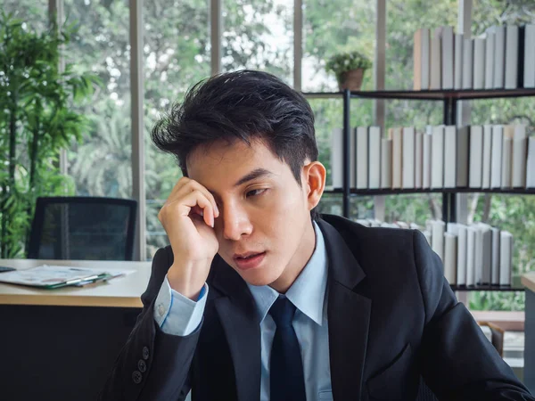 Young Asian businessman in suit with problems, tired, stressed and sad boring sitting with absent-minded on his desk in office. Frustrated worker mental health problems and burnout syndrome concept.