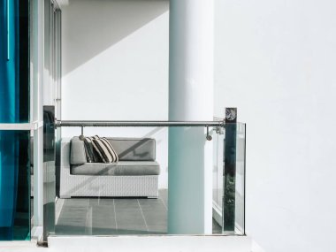 Balkonda yastıklı rahat bir rattan kanepe ve beyaz duvardaki yüksek bina arka planında cam kapının yanında fotokopi alanı olan bir teras..