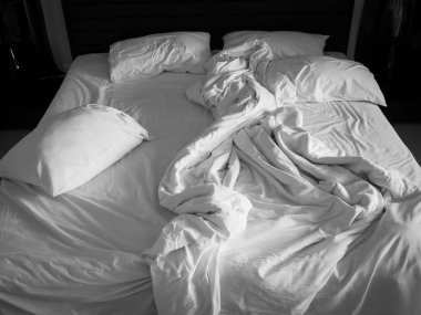 Beyaz çarşaf ve yastıklar karanlık yatak odasında dağınık. Yapılmamış yatak yastıklarla dolu.