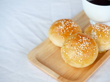 Tahta tepside beyaz susamlı taze ev yapımı hamburger çörekleri ve beyaz masa örtüsü üzerinde fotokopi alanı ile servis edilen sıcak kahve. Fırından yeni çıkmış üç lezzetli sandviç ekmeği..