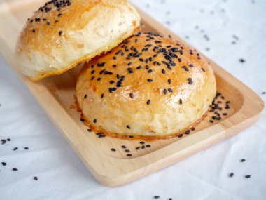 Beyaz masa örtüsü arka planında küçük tahta tepside siyah susam tohumlu ev yapımı taze hamburger çörekleri. Fırından yeni çıkmış iki lezzetli sandviçli çörek..