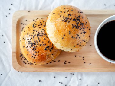 Küçük ahşap tepside siyah susamlı taze ev yapımı hamburgerler beyaz masa örtüsü üzerinde sıcak kahve servisi, üst manzara. Fırından yeni çıkmış iki lezzetli sandviçli çörek..