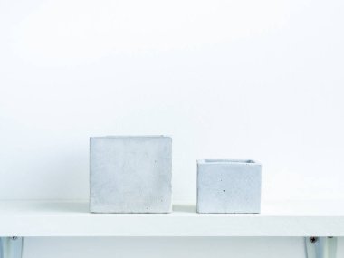 Beyaz ahşap raftaki boş, modern, geometrik beton ekicilerin iki boyutu kopya alanı olan beyaz duvar zemininde izole edilmiş. Beton kaplar, küp şeklinde..