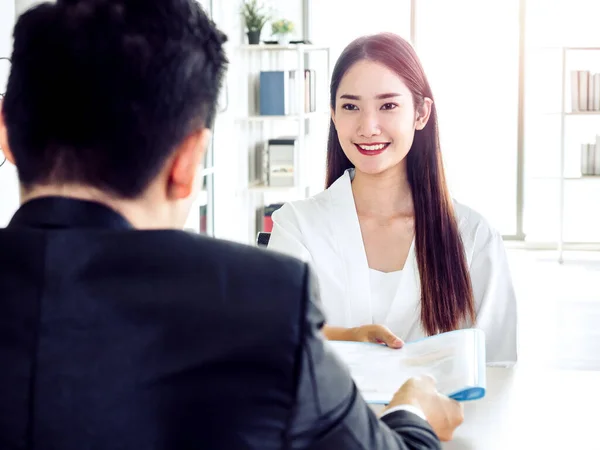 Young attractive Asian woman handing resume to businessman in suit during job interview in office. Beautiful female candidate smiling while interviewing job. Business, career and placement concept.