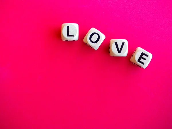 Love word written on wood block on pink red background with copy space, minimal style. Love, text is written in black letters on wooden cubes.