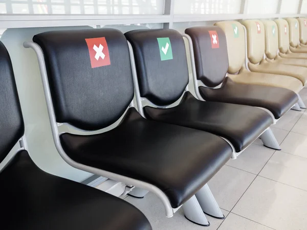 Empty waiting chairs with social distancing sign, green check mark and red cross mark. Black chairs with social distancing symbol on seat in airport during the Covid-19 or Coronavirus pandemic.