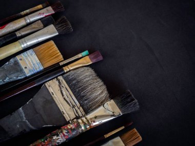 Çeşitli kullanılmış boya fırçaları. Koyu arkaplanda izole edilmiş ve kopyalama alanı olan bir sürü boyut..