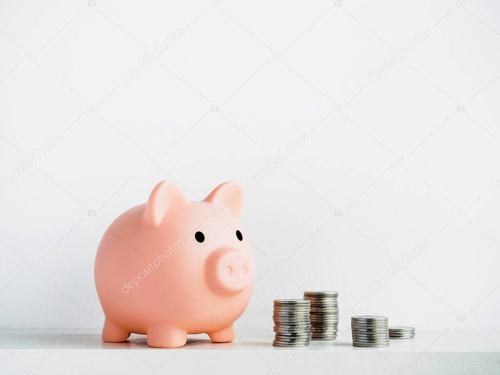 Cute piggy bank, pink color with piles of coins isolated on white background with copy space. Saving money, Investment and finance concept.