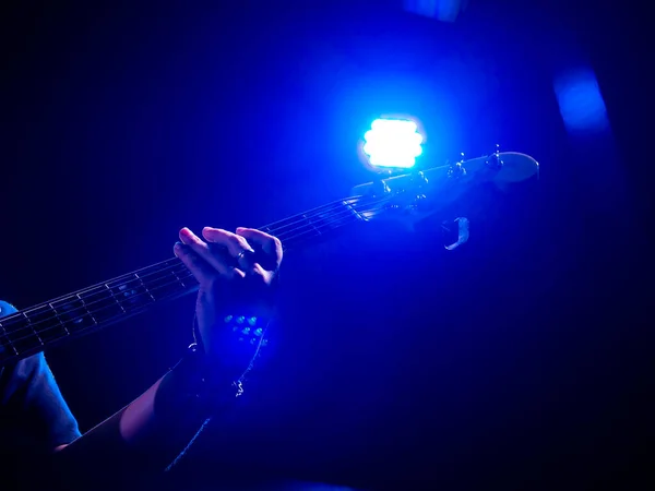 ステージ上でソロベースのギターを手で演奏し コピースペースのある暗い背景に青色の光を当てます ロックバンド コンサートで演奏するベース ギタリスト — ストック写真