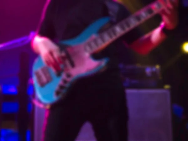 黒人のアジア系ミュージシャン ベース ギタリスト ベース ギターをステージで演奏し ダーク バックで紫色の光を放つ ロックバンドコンサートでのブリュリー音楽パフォーマンス — ストック写真