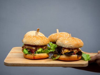 Lezzetli ev yapımı hamburger seti. El ele tutuşup, ahşap tepside ev yapımı dört hamburger veya arka planda ahşap kesme tahtası gösteriliyor..