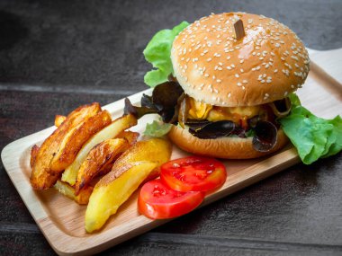 Lezzetli ev yapımı hamburger seti. Lezzetli ev yapımı hamburgerler patates kızartması ve dilimlenmiş domatesler tepside ya da ahşap masada tahta kesme tahtası.