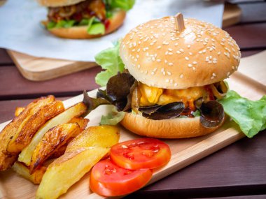 Lezzetli ev yapımı hamburger seti. Lezzetli ev yapımı hamburgerler patates kızartması ve dilimlenmiş domatesler tepside ya da ahşap masada tahta kesme tahtası.