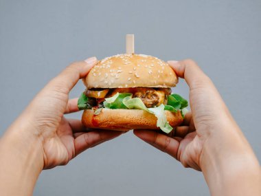 Delicious fresh homemade burger. hands holding tasty homemade hamburger on grey background. Hand showing beef burger.