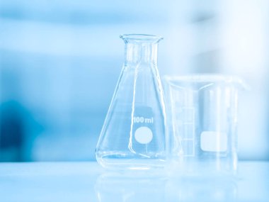 Boş cam matara 100 ml ve fotokopi uzayı ile ilgili bir bilim deneyi için mavi kimya laboratuvarı arka planında ölçüm kabı. Bilimsel ekipman ve eğitim konsepti.