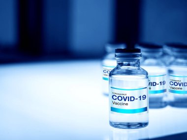 Covid-19 aşısı. Modern etiket Covid-19 şişedeki aşılar ışık masasını aydınlatan mavi tonlu bir laboratuvar. Bir koronavirüs aşısı geliştirilmesi ve oluşturulması.