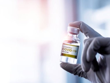 Covid-19 aşısı. Laboratuvarda fotokopi alanı olan eldiven giyen bir bilim adamı ya da doktorun şişe şişesi üzerindeki modern etiket Covid-19 aşısı. Coronavirüs aşısının geliştirilmesi ve yaratılması.