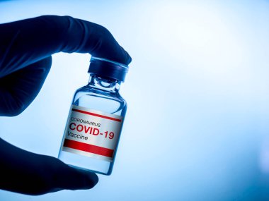 Covid-19 aşısı. Laboratuvarda eldiven takan bilim adamı ya da doktorun şişe şişesi üzerindeki modern kırmızı etiket Covid-19 aşısı, koyu mavi ton. Coronavirüs aşısının geliştirilmesi ve yaratılması.