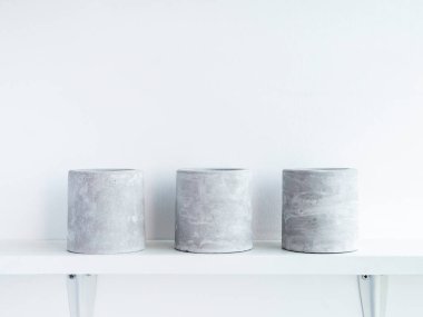 Beyaz ahşap bir raftaki üç adet boş, yuvarlak beton saksı kopya alanı olan beyaz duvar zemininde izole edilmiş. Kaktüs, sulu bitkiler ya da çiçekler için küçük çimento ekicisi..