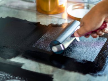 Sanatçı elinin hareket bulanıklığı, baskı makinesi resim stüdyosunda siyah mürekkep renginde rulo yapıyor, kapat. Linocut, ahşap kesim, oyma ve ipekten resim yazdırma işlemi.
