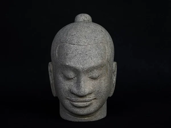 Head of Buddha carved from stone isolated on dark background. Face of antique stone buddha, front view.