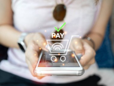 İnternetten alışveriş konsepti. Cep telefonuyla bağlantısız ödeme. Kablosuz ödemesi ve alışveriş arabası ikonu olan akıllı telefon kullanan yakın plan kadın eli..