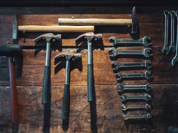 Set of wrench and old hammers hanging on wooden wall background, vertical style. Many size of wrenches and hammers on wood plank wall.