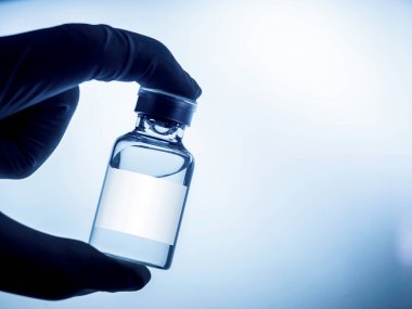 Bilim adamının elinde beyaz boş etiketli tıbbi aşı şişesi fotokopi alanı olan lastik eldivenlerle, koyu mavi tonda. İğne için cam aşı şişesi tutan el resmini kapat.