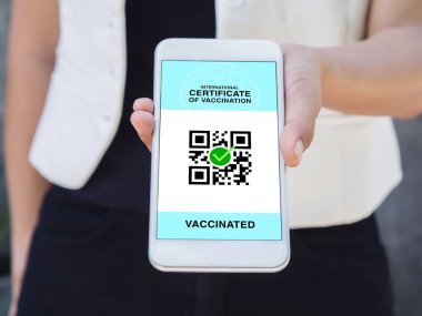 Uluslararası aşı sertifikası, akıllı dijital pasaport ve akıllı telefon ekranında QR kodu. Aşılanmış kadın eli, aşı sertifikası için sağlık pasaportu gösteriyor..