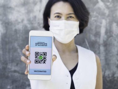 Uluslararası aşı sertifikası, akıllı dijital pasaport ve akıllı telefon ekranında QR kodu. Aşılanmış, bandajlı Asyalı kadın aşı sertifikası için sağlık pasaportu gösteriyor..