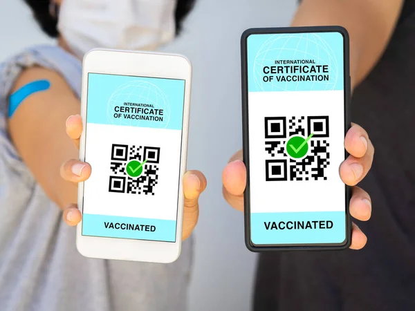 International certificate of vaccination, smart digital passport with QR code on smartphone screen. Vaccinated man and woman wearing face mask showing health passport of vaccination certification.