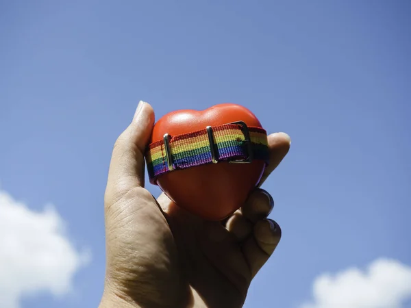ゲイの人々が青い空の背景に手に赤いハートボールに小さな虹の旗ベルト プライドカラーとレインボーフラッグストリップとLgbtの概念 — ストック写真