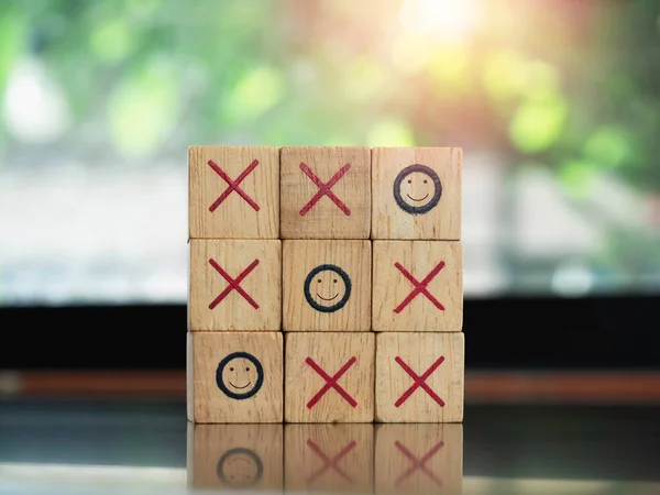 Three smiling face icons on tic tac toe wooden block game on wood table on green nature background. Winner, strategy and business goal concept.