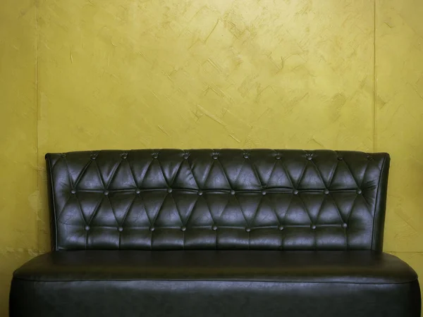 Dark green vintage leather sofa seat with pins and buttons on yellow wall background in the living room with copy space.